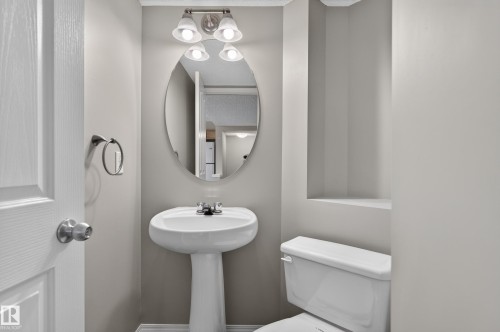 Pedestal sink with chrome faucet, oval mirror, and wall-mounted vanity lighting - 6008 South Terwillegar Boulevard Nw, Edmonton, AB - Indoor Photo Showing Bathroom