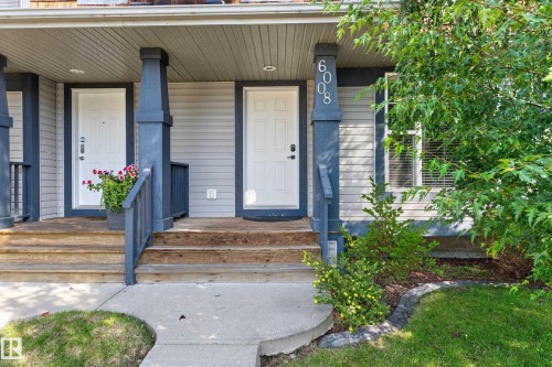 Front entry with light gray siding and white door, featuring wood stairs, dark blue railings, and a concrete walkway - 6008 South Terwillegar Boulevard Nw, Edmonton, AB - Outdoor