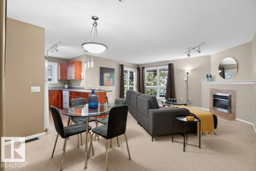 Open-concept living area featuring a fireplace, multiple windows, kitchen with wood-finish cabinetry, and a dedicated dining space with pendant lighting - #201 10528 77 Av Nw, Edmonton, AB - Indoor With Fireplace