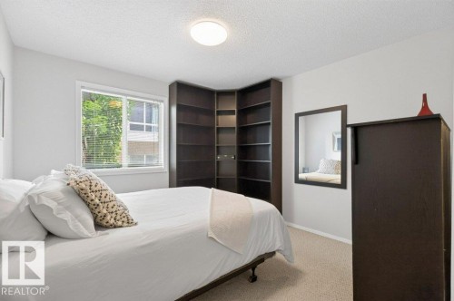 Window with blinds, wall-mounted mirror, built-in corner shelving, overhead flush-mount lighting, and wall-to-wall carpeting - #201 10528 77 Av Nw, Edmonton, AB - Indoor Photo Showing Bedroom