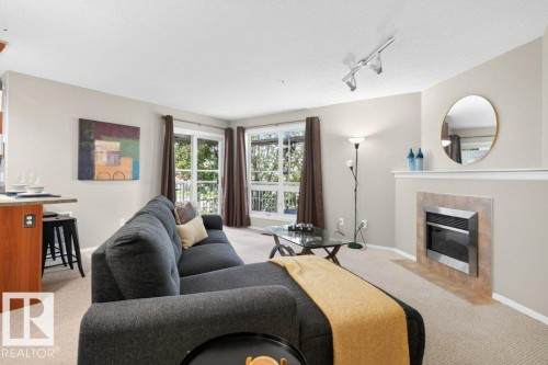 Recessed fireplace with tile surround, carpeted flooring, track lighting, and built-in shelving - #201 10528 77 Av Nw, Edmonton, AB - Indoor Photo Showing Living Room With Fireplace