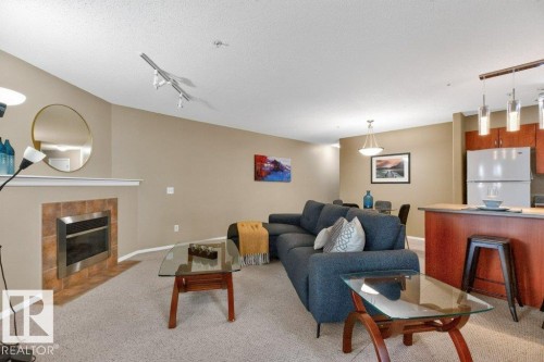 Living area with a tiled fireplace, vaulted ceiling, track lighting, and carpet flooring - #201 10528 77 Av Nw, Edmonton, AB - Indoor Photo Showing Living Room With Fireplace