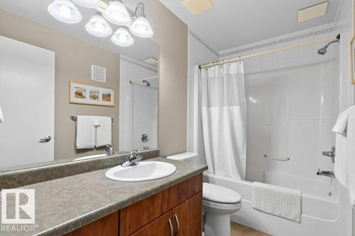 Bathroom featuring a vanity with a surface-mounted sink, wood-finish cabinetry, a large mirror, and a built-in bathtub with shower - #201 10528 77 Av Nw, Edmonton, AB - Indoor Photo Showing Bathroom
