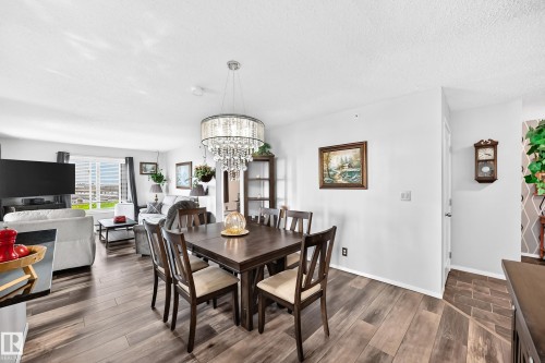 Hardwood-finish flooring throughout, a modern chandelier with crystal accents, and a large window offering natural light - #401 5390 Chappelle Rd Sw, Edmonton, AB 
