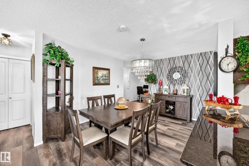 Wood-finish flooring throughout, a geometric accent wall, and a crystal chandelier - #401 5390 Chappelle Rd Sw, Edmonton, AB 