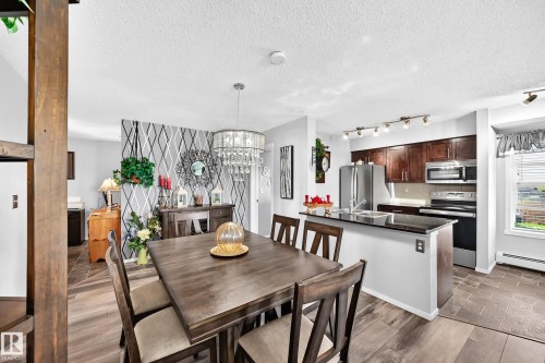 Modern kitchen featuring wood cabinetry, stainless steel appliances, and a black countertop - #401 5390 Chappelle Rd Sw, Edmonton, AB 