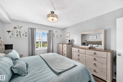 Textured ceiling with a central drum light fixture, light gray walls, window with horizontal blinds, and wood-finish flooring - #401 5390 Chappelle Rd Sw, Edmonton, AB 