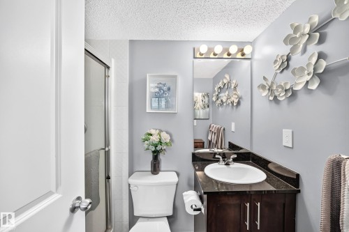 Enclosed shower with a glass door, vanity with an integrated sink, dark countertop, and wood-finish cabinetry - #401 5390 Chappelle Rd Sw, Edmonton, AB 