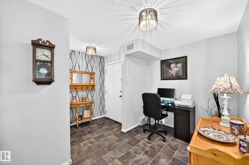 Foyer featuring slate-look tile flooring, contemporary flush-mount lighting, and an accent wall with a geometric pattern - #401 5390 Chappelle Rd Sw, Edmonton, AB 