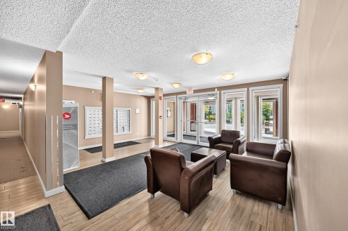 Welcoming lobby featuring recessed ceiling lighting, wood-finish flooring, and multiple glass-paneled entrance doors with transom windows - #401 5390 Chappelle Rd Sw, Edmonton, AB 