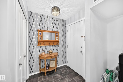 Textured tile flooring, patterned accent wall, white paneled doors, and a decorative ceiling light fixture - #401 5390 Chappelle Rd Sw, Edmonton, AB 