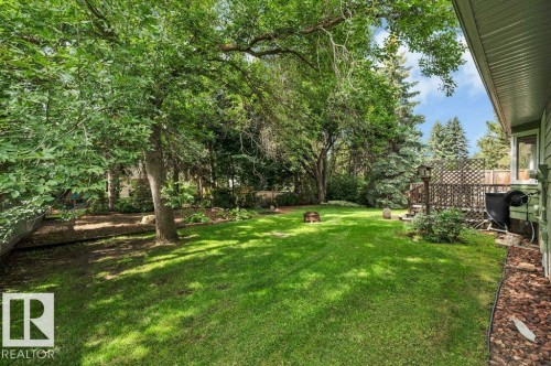 Expansive backyard featuring a manicured lawn, mature trees, and a raised wooden deck with lattice detailing - 5620 151 Street Nw, Edmonton, AB - Outdoor