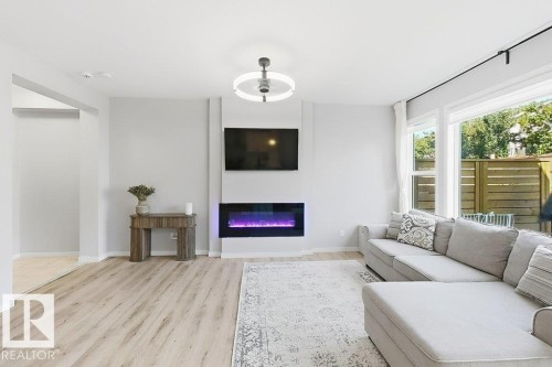 Bright living area featuring wood-finish flooring, an electric fireplace, a modern ceiling light fixture, and large windows - 4242 Chichak Close Sw, Edmonton, AB - Indoor Photo Showing Living Room With Fireplace