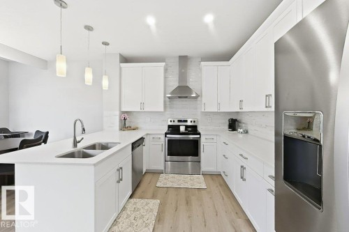 Kitchen featuring white cabinetry, light countertops, wood-finish flooring, stainless steel appliances, and a tiled backsplash - 4242 Chichak Close Sw, Edmonton, AB - Indoor Photo Showing Kitchen With Double Sink With Upgraded Kitchen