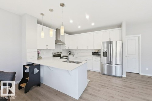 Kitchen featuring white shaker cabinetry, stainless steel appliances, a white tile backsplash, and wood-finish flooring - 4242 Chichak Close Sw, Edmonton, AB - Indoor Photo Showing Kitchen With Double Sink With Upgraded Kitchen