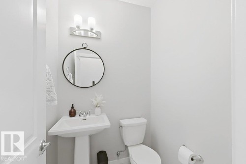 Pedestal sink with chrome faucet, circular wall mirror, and modern vanity light fixture - 4242 Chichak Close Sw, Edmonton, AB - Indoor Photo Showing Bathroom