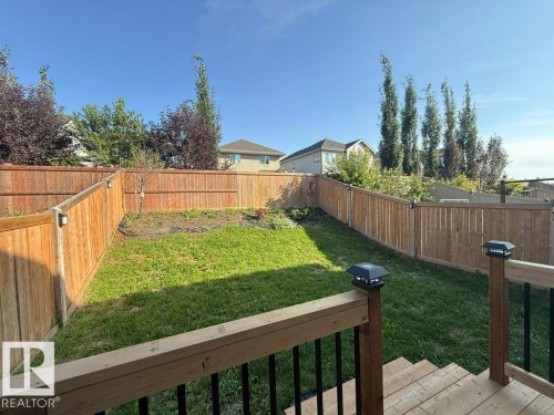 Expansive outdoor space featuring a wood fence, green lawn, deck with steps, and rail lighting - 4242 Chichak Close Sw, Edmonton, AB - Outdoor With Backyard