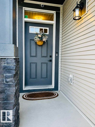 Entry with a panel door, transom window, and exterior wall lantern - 4242 Chichak Close Sw, Edmonton, AB - Outdoor With Exterior