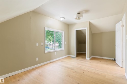 Light wood-finish flooring with white trim, window offering natural light, two ceiling-mounted light fixtures, and a white interior door - 12337 128 Avenue Nw, Edmonton, AB - Indoor Photo Showing Other Room