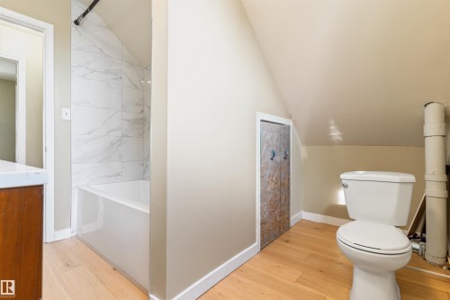 Contemporary bathroom featuring a white bathtub, marble-look tiled shower surround, light wood-finish flooring, and a white toilet - 12337 128 Avenue Nw, Edmonton, AB - Indoor Photo Showing Bathroom