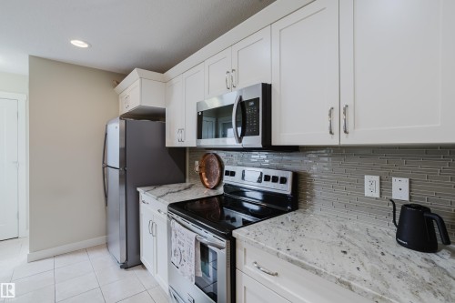 Kitchen featuring white cabinetry, stainless steel appliances, speckled countertops, a glass tile backsplash, and light-toned floor tiling - 124 Cy Becker Boulevard Nw, Edmonton, AB - Indoor Photo Showing Kitchen With Stainless Steel Kitchen