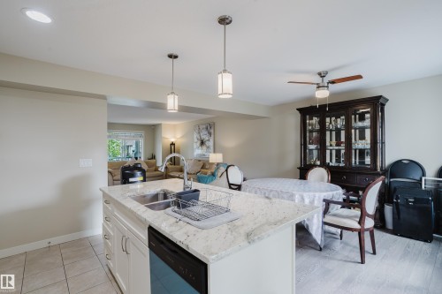 Kitchen island featuring an undermount double basin sink with a high-arc faucet, integrated dishwasher, and light-toned solid surface countertop - 124 Cy Becker Boulevard Nw, Edmonton, AB - Indoor Photo Showing Kitchen With Double Sink