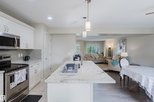 Kitchen featuring an expansive island with a stainless steel sink, pendant lighting, white cabinetry, stainless steel appliances, and wood-finish flooring - 124 Cy Becker Boulevard Nw, Edmonton, AB - Indoor Photo Showing Kitchen With Stainless Steel Kitchen With Upgraded Kitchen