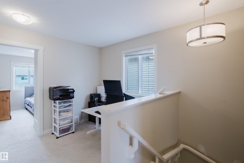 Carpeted upper-level landing featuring a built-in half-wall desk with a window, a contemporary pendant light fixture, and a flush-mount ceiling light - 124 Cy Becker Boulevard Nw, Edmonton, AB - Indoor