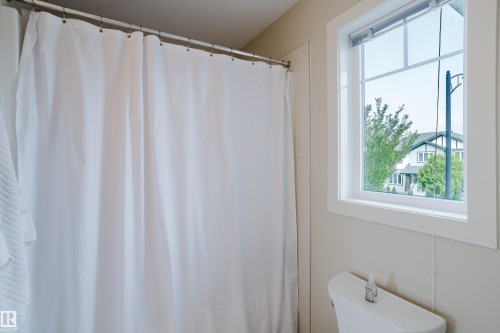 Bathroom featuring a window with white trim, a toilet, and a shower area with a white shower curtain on a silver rod - 124 Cy Becker Boulevard Nw, Edmonton, AB - Indoor Photo Showing Bathroom