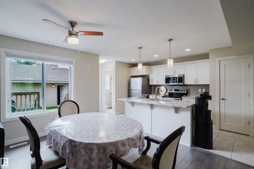 Open-concept kitchen and dining area featuring white cabinetry, stainless steel appliances, a kitchen island with pendant lighting, and wood-finish flooring - 124 Cy Becker Boulevard Nw, Edmonton, AB - Indoor