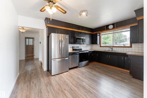 Kitchen featuring wood-finish flooring, stainless steel appliances, dark cabinetry with wood trim, and a tile backsplash - 7120 139 Avenue Nw, Edmonton, AB - Indoor Photo Showing Kitchen