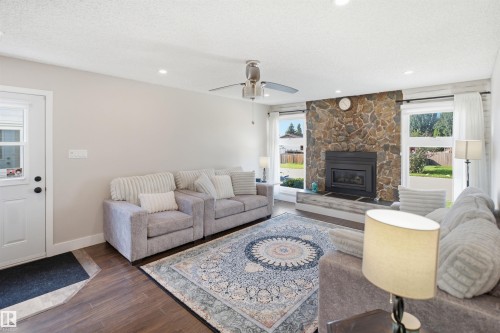 Stone-faced fireplace with a built-in firebox, wood-finish flooring, recessed lighting, ceiling fan, and multiple windows with white trim - 3515 20 Ave Nw, Edmonton, AB - Indoor Photo Showing Living Room With Fireplace