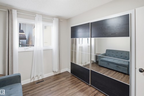 Wood-finish flooring, white walls, and a window with white trim, complemented by a mirrored closet with dark wood-grain panels - 3515 20 Ave Nw, Edmonton, AB - Indoor Photo Showing Other Room