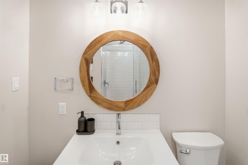 Bathroom featuring a circular wood-framed mirror, undermount sink, and polished chrome faucet - 3515 20 Ave Nw, Edmonton, AB - Indoor Photo Showing Bathroom