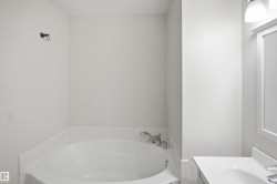 Corner soaking tub with polished chrome fixtures and an adjacent vanity featuring a rectangular sink, white countertop, and a framed mirror with overhead lighting - 