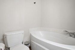 White built-in bathtub with deck-mounted chrome fixtures, white toilet, and light-colored walls - 