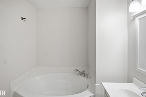 Corner soaking tub with polished chrome fixtures and an adjacent vanity featuring a rectangular sink, white countertop, and a framed mirror with overhead lighting - 3515 20 Ave Nw, Edmonton, AB - Indoor Photo Showing Bathroom