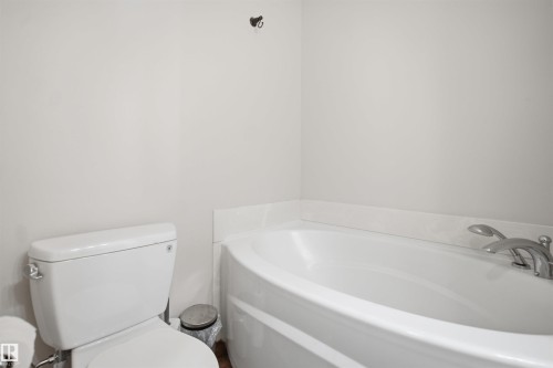 White built-in bathtub with deck-mounted chrome fixtures, white toilet, and light-colored walls - 3515 20 Ave Nw, Edmonton, AB - Indoor Photo Showing Bathroom