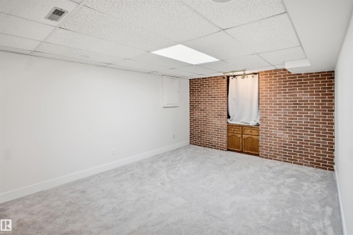 Spacious room featuring new carpeting, white painted walls, a brick-finish accent wall, built-in wood cabinetry, and a drop ceiling with integrated lighting - 3515 20 Ave Nw, Edmonton, AB - Indoor