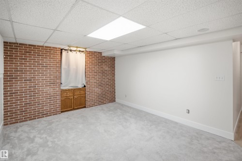 Textured brick accent wall, built-in wooden cabinetry, soft gray carpet, and a drop ceiling with integrated lighting - 3515 20 Ave Nw, Edmonton, AB - Indoor Photo Showing Other Room