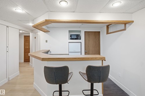 Built-in bar with wood-finish countertop, recessed lighting, integrated microwave, compact refrigerator, and wood-finish flooring - 3515 20 Ave Nw, Edmonton, AB - Indoor