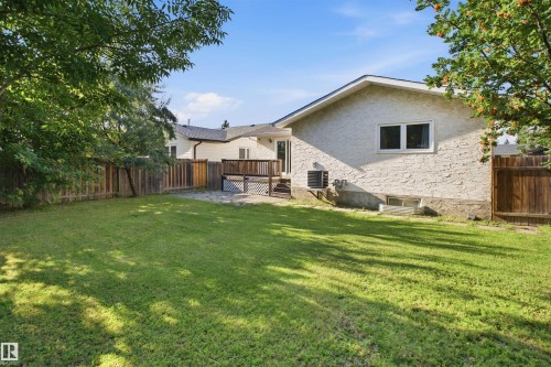 Expansive grassy yard with mature trees, a wooden fence, and a multi-level deck with white lattice details - 3515 20 Ave Nw, Edmonton, AB - Outdoor