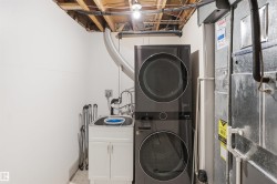 Stackable washer and dryer, laundry sink with white cabinet, exposed ceiling joists, and utility access - 