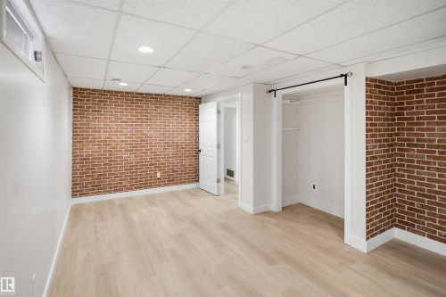Light wood-finish flooring with a brick-finish accent wall - 3515 20 Ave Nw, Edmonton, AB - Indoor Photo Showing Other Room