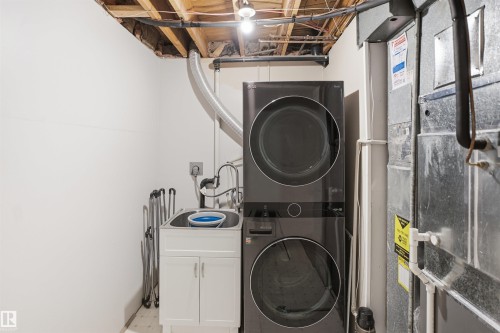 Stackable washer and dryer, laundry sink with white cabinet, exposed ceiling joists, and utility access - 3515 20 Ave Nw, Edmonton, AB - Indoor Photo Showing Laundry Room