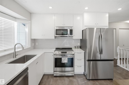 Modern kitchen featuring white cabinetry, stainless steel appliances, a bay window, a single basin sink, and wood-finish flooring - 3515 20 Ave Nw, Edmonton, AB - Indoor Photo Showing Kitchen With Upgraded Kitchen