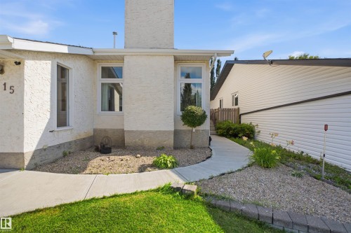 Stucco exterior with a prominent chimney feature, white window frames, concrete pathway, and gravel landscaping - 3515 20 Ave Nw, Edmonton, AB - Outdoor