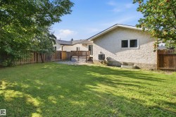 Expansive grassy yard with mature trees, a wooden fence, and a multi-level deck with white lattice details - 