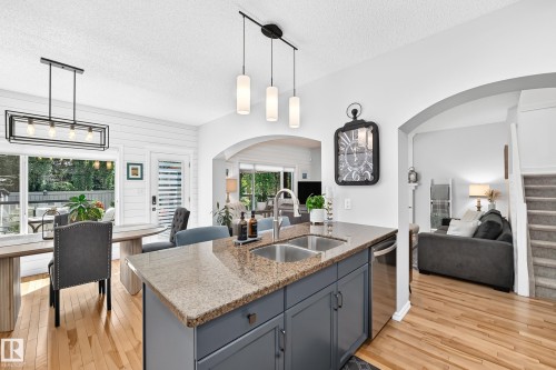 Kitchen island featuring a granite countertop, dual stainless steel sinks, and dark gray cabinetry - 823 77 Street Sw, Edmonton, AB - Indoor Photo Showing Other Room