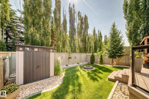 Manicured backyard with a built-in fire pit, composite decking, and mature perimeter trees - 823 77 Street Sw, Edmonton, AB - Outdoor With Backyard